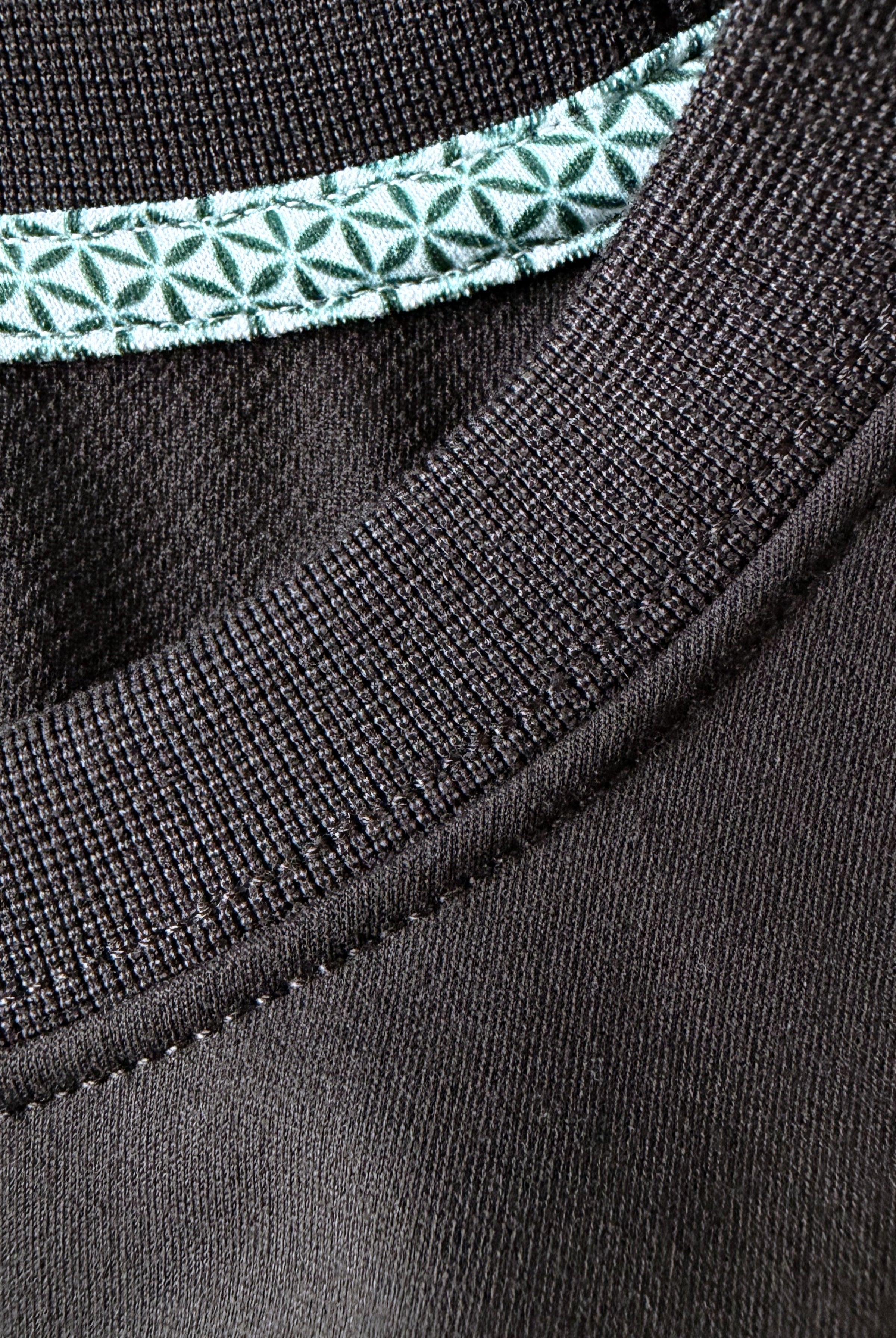 Close-up view of TARANIRVANA Essenza T-Shirt crewneck in Phantom black, highlighting the premium ribbed collar, green geometric pattern inner trim, and high-performance SpiroTex™ fabric with quick-dry, moisture-wicking, odor-resistant, and UPF 50+ sun protection.