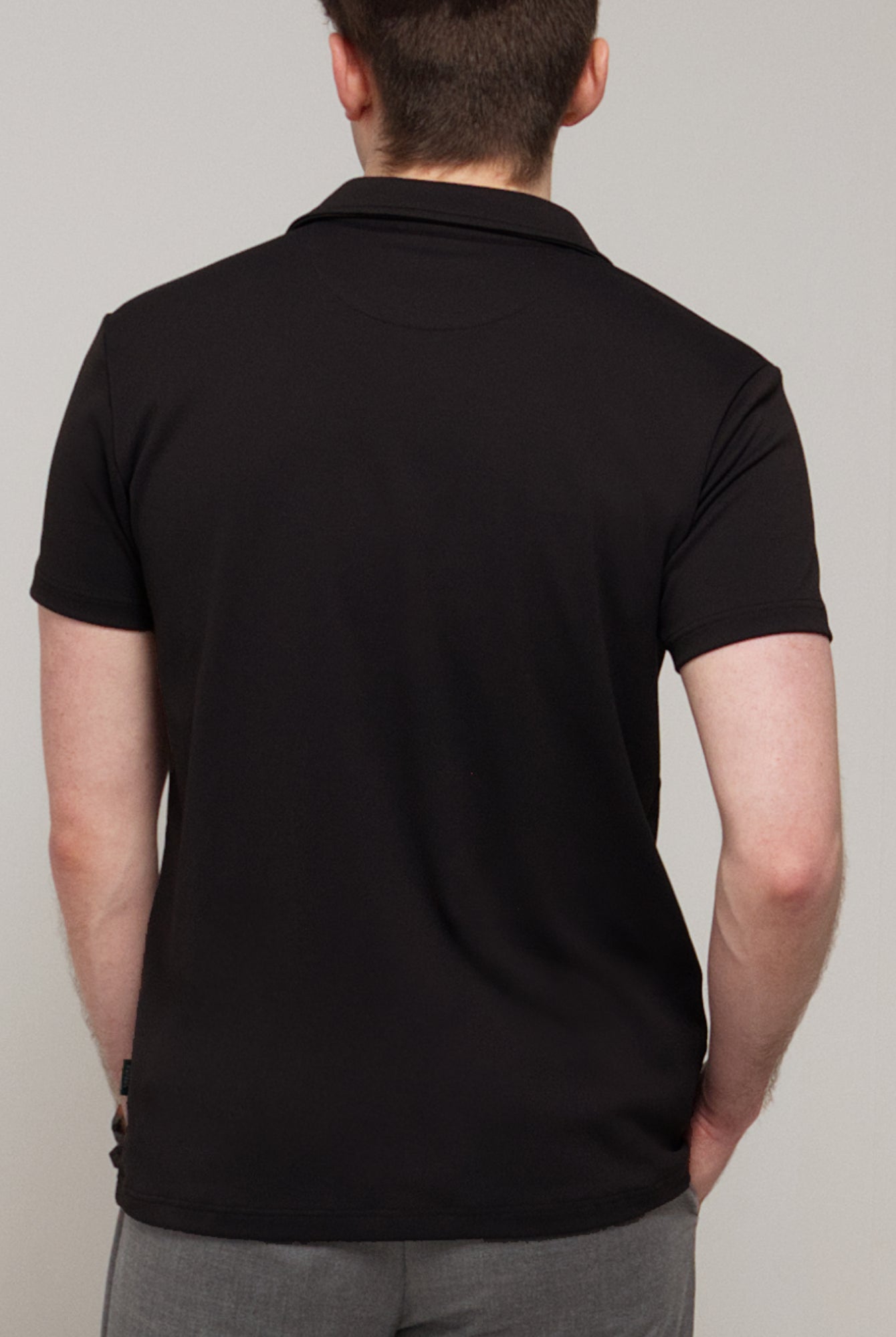 Back view of a man wearing TARANIRVANA Aria Polo in Phantom black, showing the clean tailored shoulders and high-performance SpiroTex™ fabric with quick-dry, moisture-wicking, odor-resistant, and UPF 50+ sun protection.