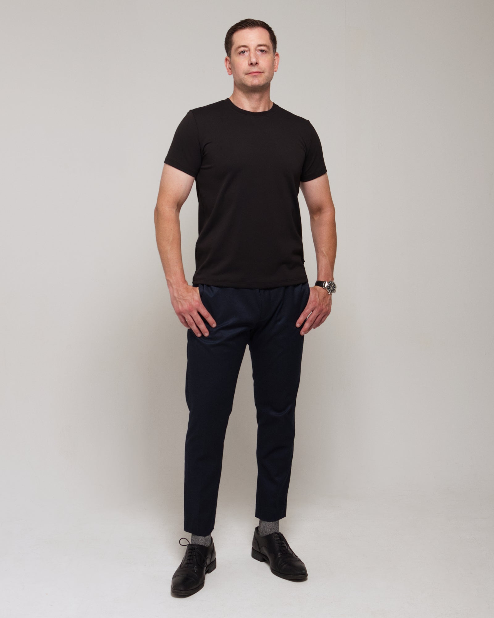 Front view of a man wearing TARANIRVANA Essenza T-Shirt in Phantom black, showcasing the classic crewneck and high-performance SpiroTex™ fabric with quick-dry, moisture-wicking, odor-resistant, and UPF 50+ sun protection.