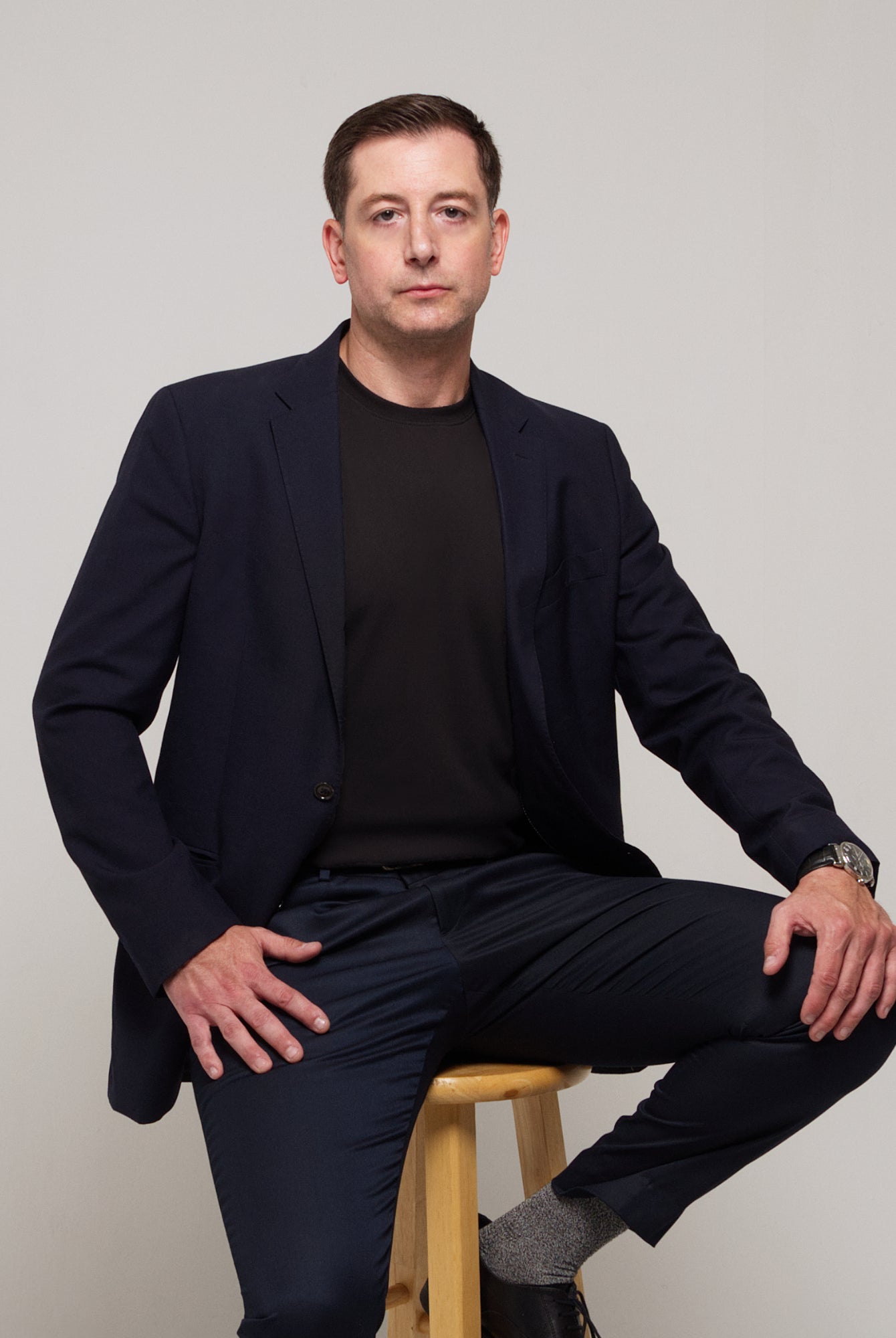 Front view of a man styling TARANIRVANA Essenza T-Shirt in Phantom black layered under a sharp navy business suit jacket, featuring premium SpiroTex fabric with quick-dry, moisture-wicking, odor-resistant, and UPF 50+ sun protection.