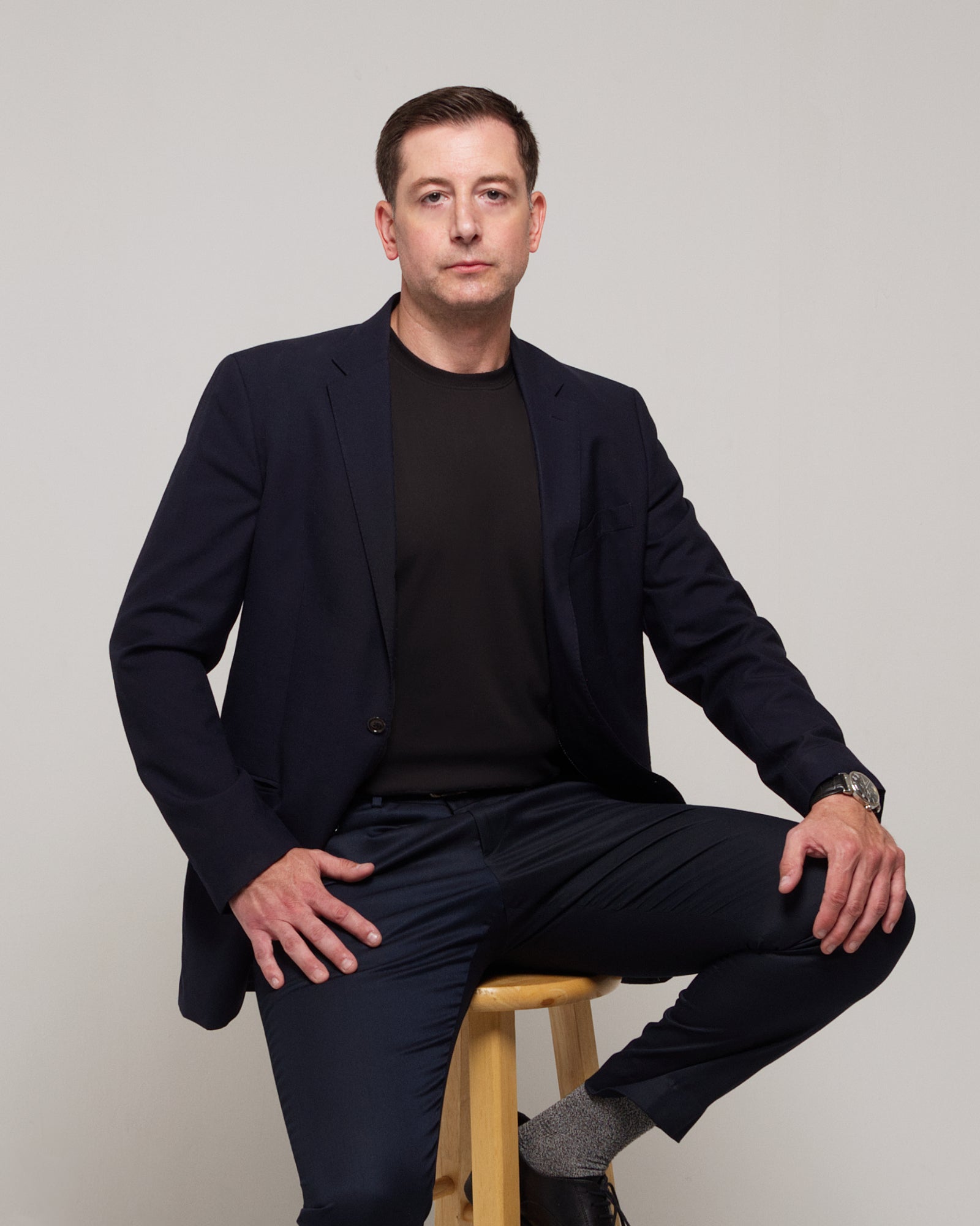 Front view of a man styling TARANIRVANA Essenza T-Shirt in Phantom black layered under a sharp navy business suit jacket, featuring premium SpiroTex fabric with quick-dry, moisture-wicking, odor-resistant, and UPF 50+ sun protection.