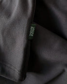 Close-up view of TARANIRVANA Aria Polo shirt hem in Phantom black, highlighting the premium stitching and signature green brand woven label with quick-dry, moisture-wicking, odor-resistant, and UPF 50+ sun protection.