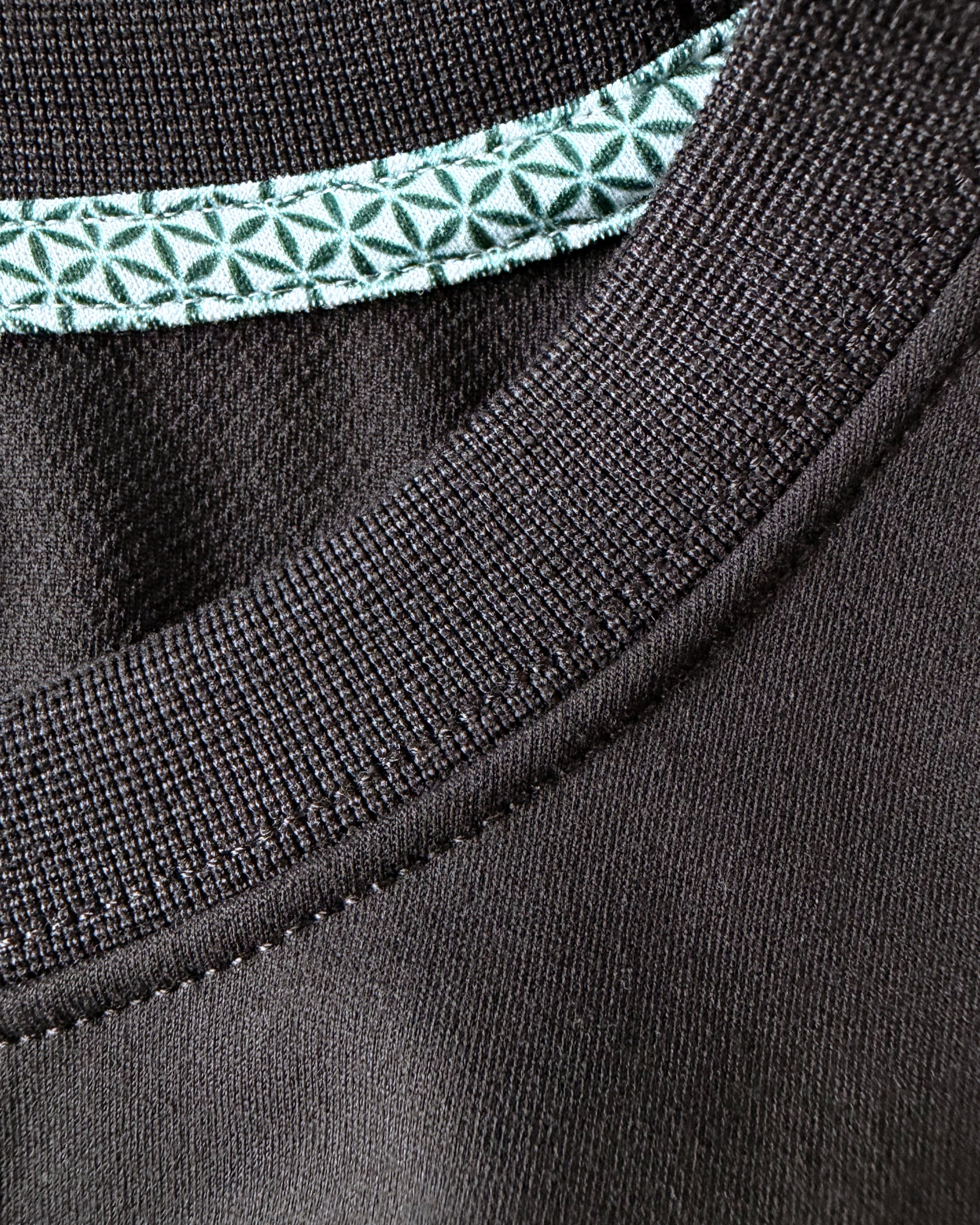 Close-up view of TARANIRVANA Essenza T-Shirt crewneck in Phantom black, highlighting the premium ribbed collar, green geometric pattern inner trim, and high-performance SpiroTex™ fabric with quick-dry, moisture-wicking, odor-resistant, and UPF 50+ sun protection.