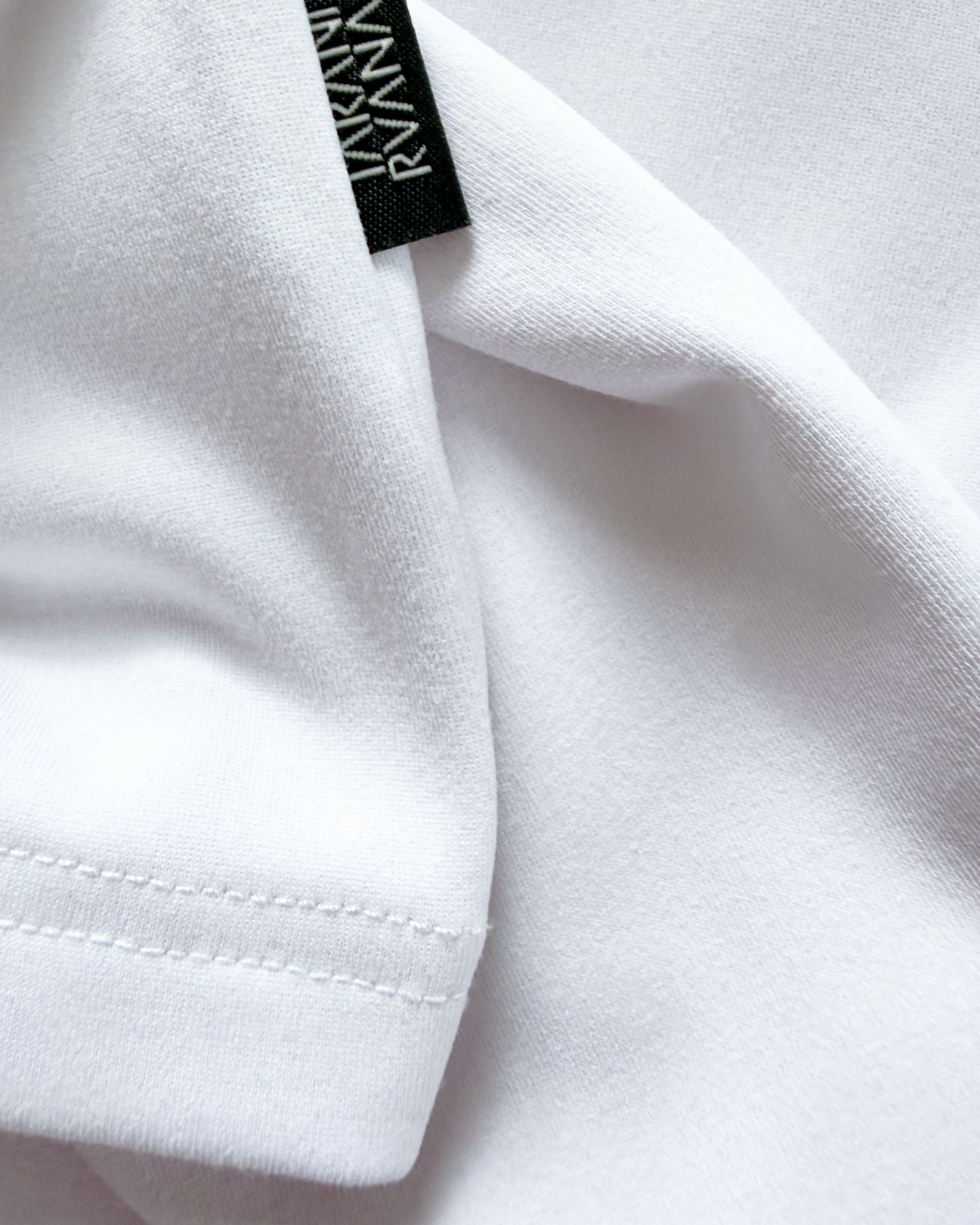 Macro close-up of TARANIRVANA Porcelain white garment, highlighting premium SpiroTex™ fabric texture, refined stitching, and black brand woven label with quick-dry, moisture-wicking, odor-resistant, and UPF 50+ sun protection.