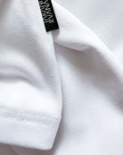 Macro close-up of TARANIRVANA Porcelain white garment, highlighting premium SpiroTex™ fabric texture, refined stitching, and black brand woven label with quick-dry, moisture-wicking, odor-resistant, and UPF 50+ sun protection.