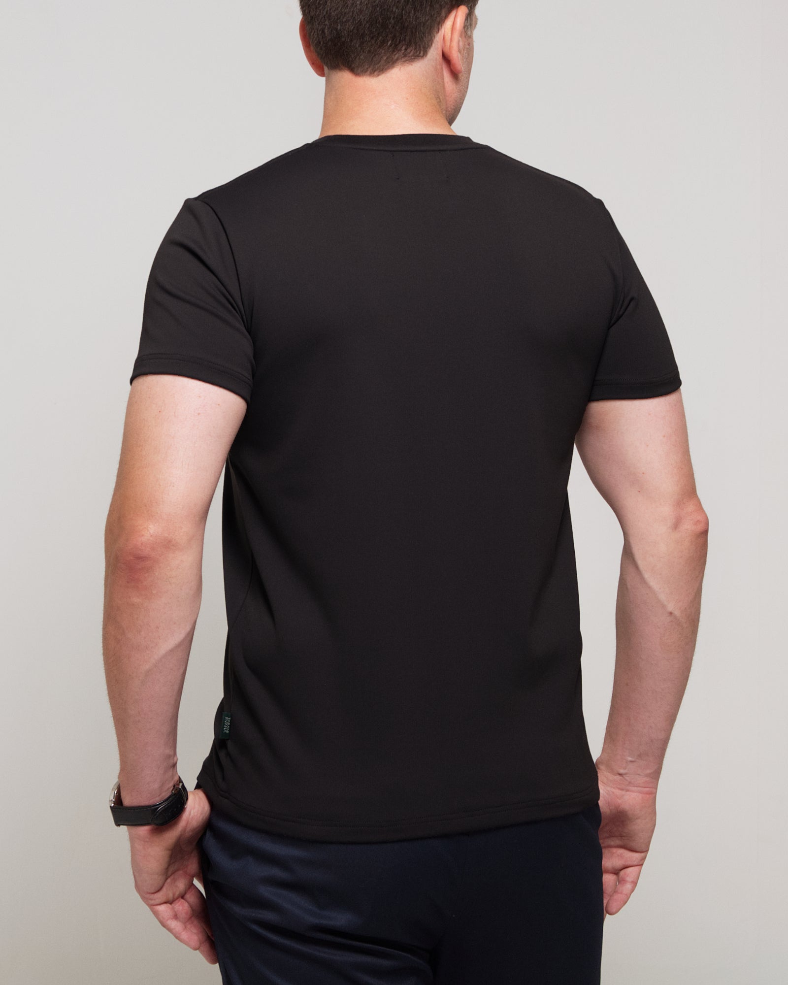 Back view of a man wearing TARANIRVANA Essenza T-Shirt in Phantom black, showcasing clean tailored shoulders and high-performance SpiroTex™ fabric with quick-dry, moisture-wicking, odor-resistant, and UPF 50+ sun protection.