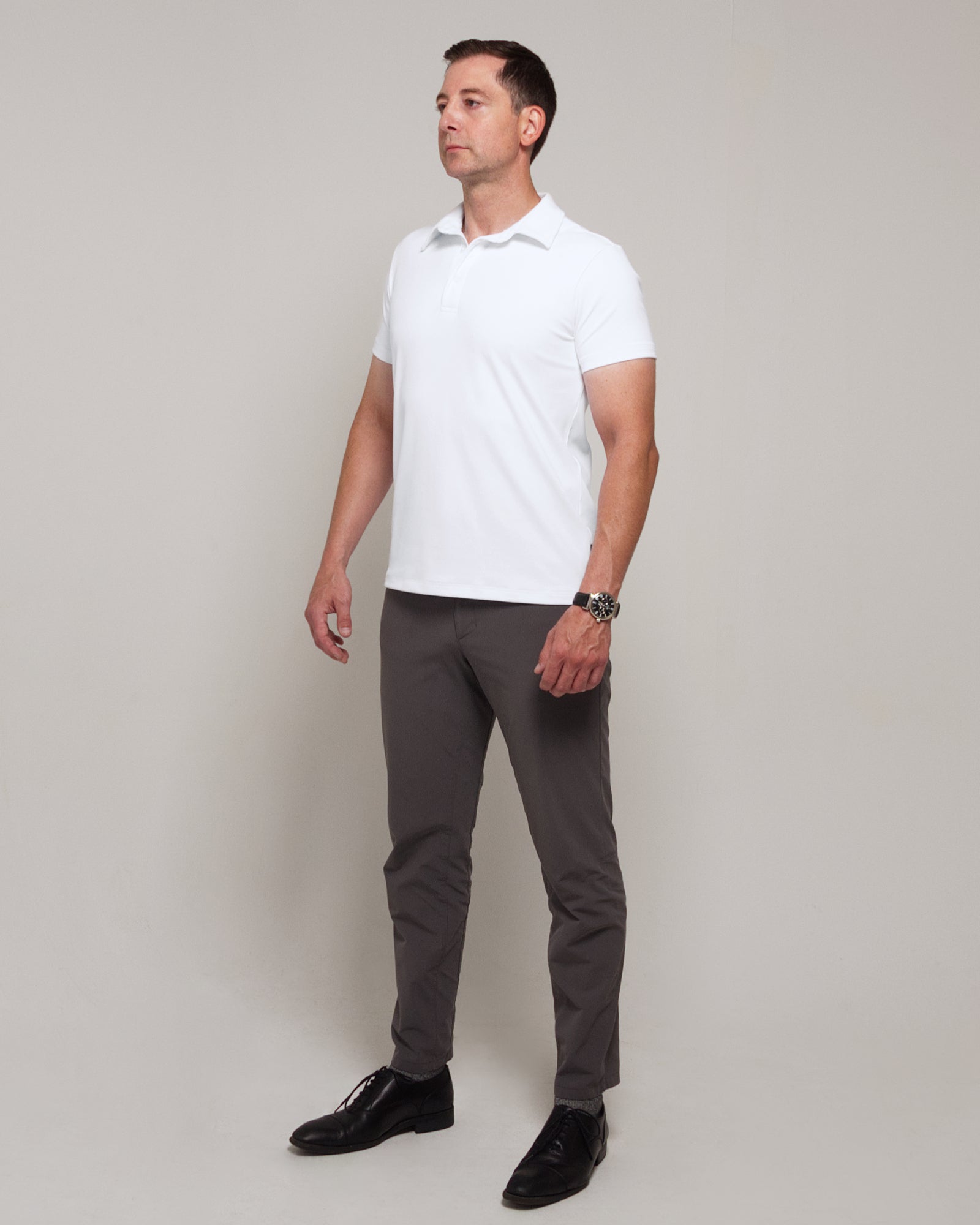 Full-length three-quarter view of a man wearing TARANIRVANA Aria Polo in Porcelain white, showcasing a sophisticated smart business silhouette in high-performance SpiroTex™ fabric with quick-dry, moisture-wicking, odor-resistant, and UPF 50+ sun protection.