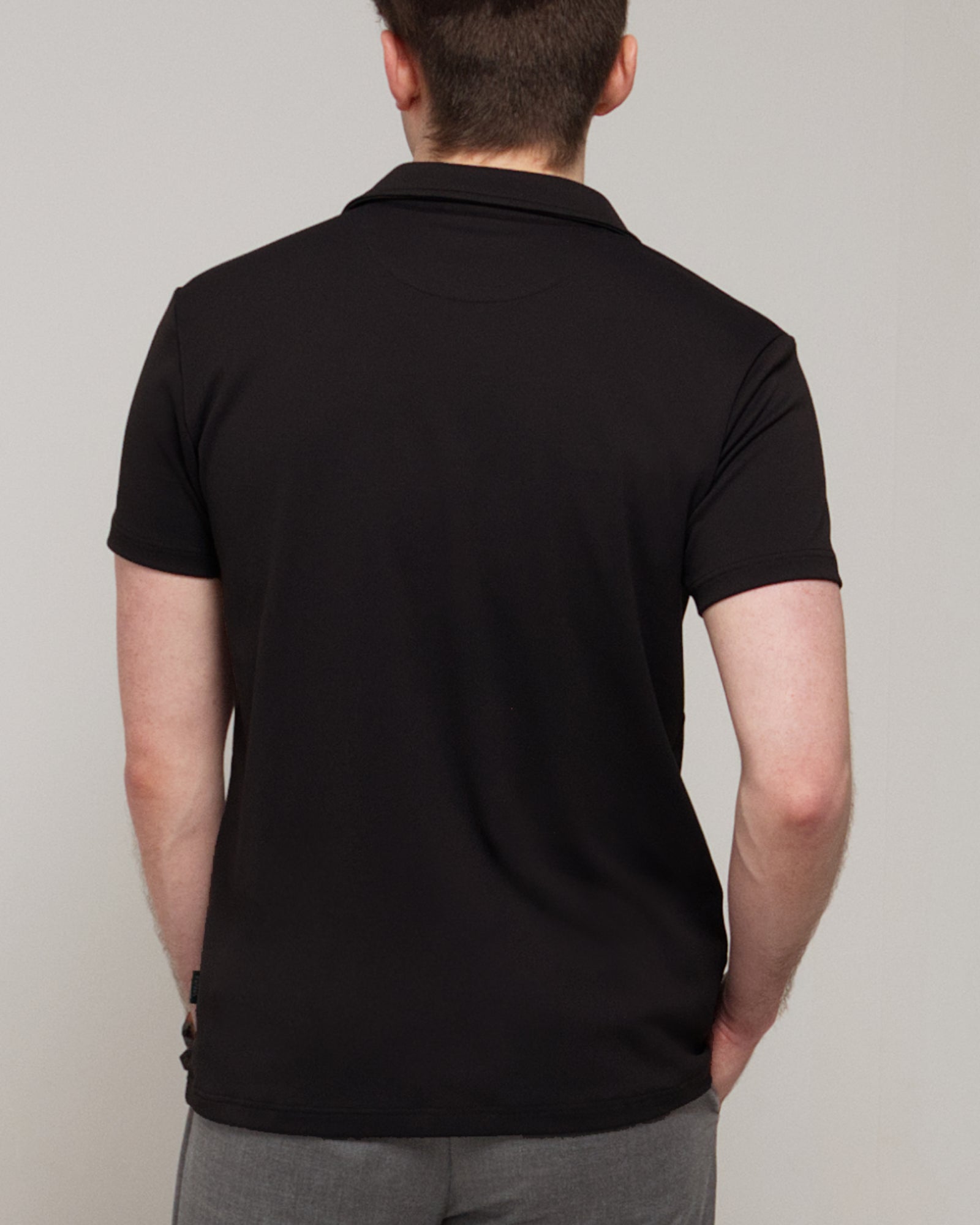 Back view of a man wearing TARANIRVANA Aria Polo in Phantom black, showing the clean tailored shoulders and high-performance SpiroTex™ fabric with quick-dry, moisture-wicking, odor-resistant, and UPF 50+ sun protection.